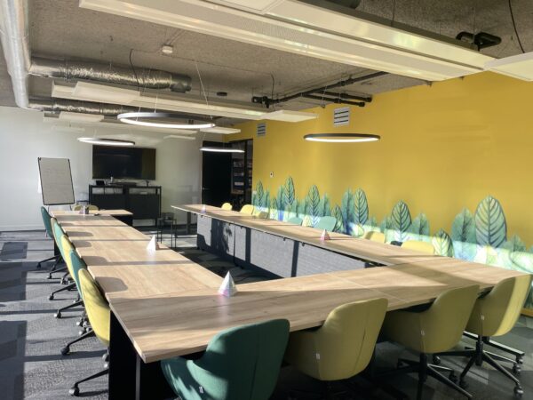 Vergaderruimte aan de Jan Leentvaarlaan met U-vormige opstelling, gele muur met bladmotief en moderne kantoorstoelen.